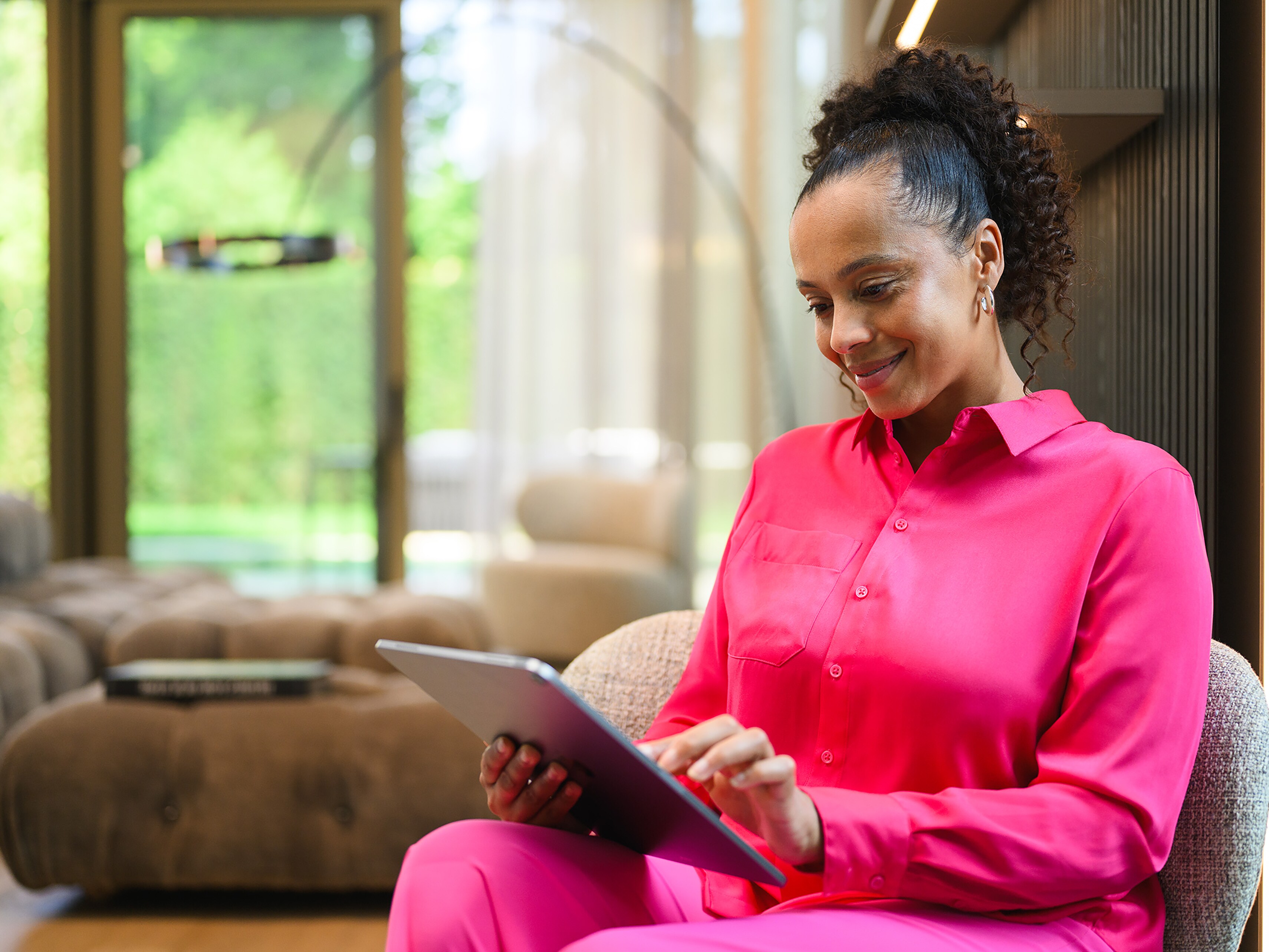 Woman in bright pink clothing using a tablet in a living room