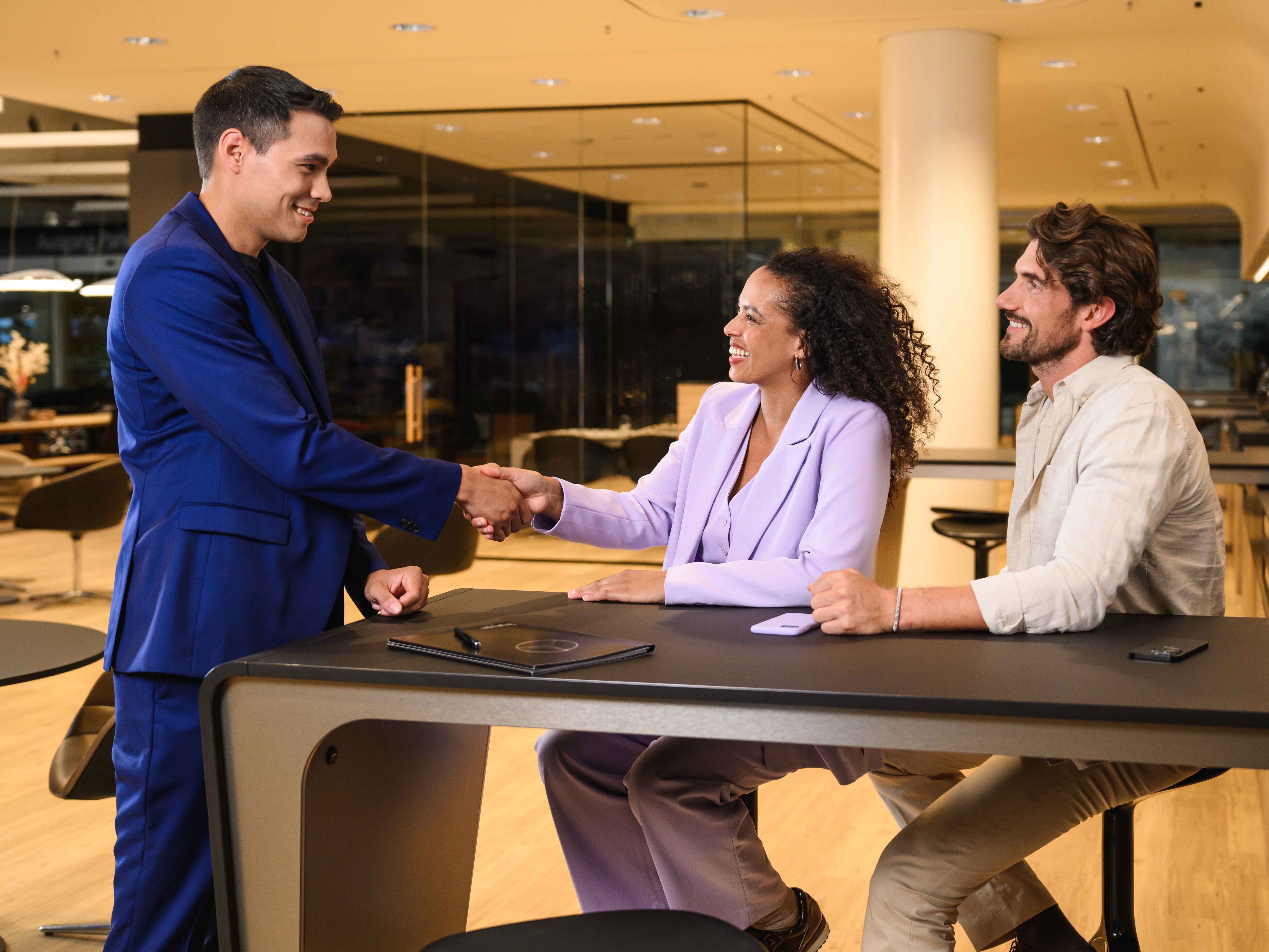 Three colleagues shaking hands across a showroom desk.