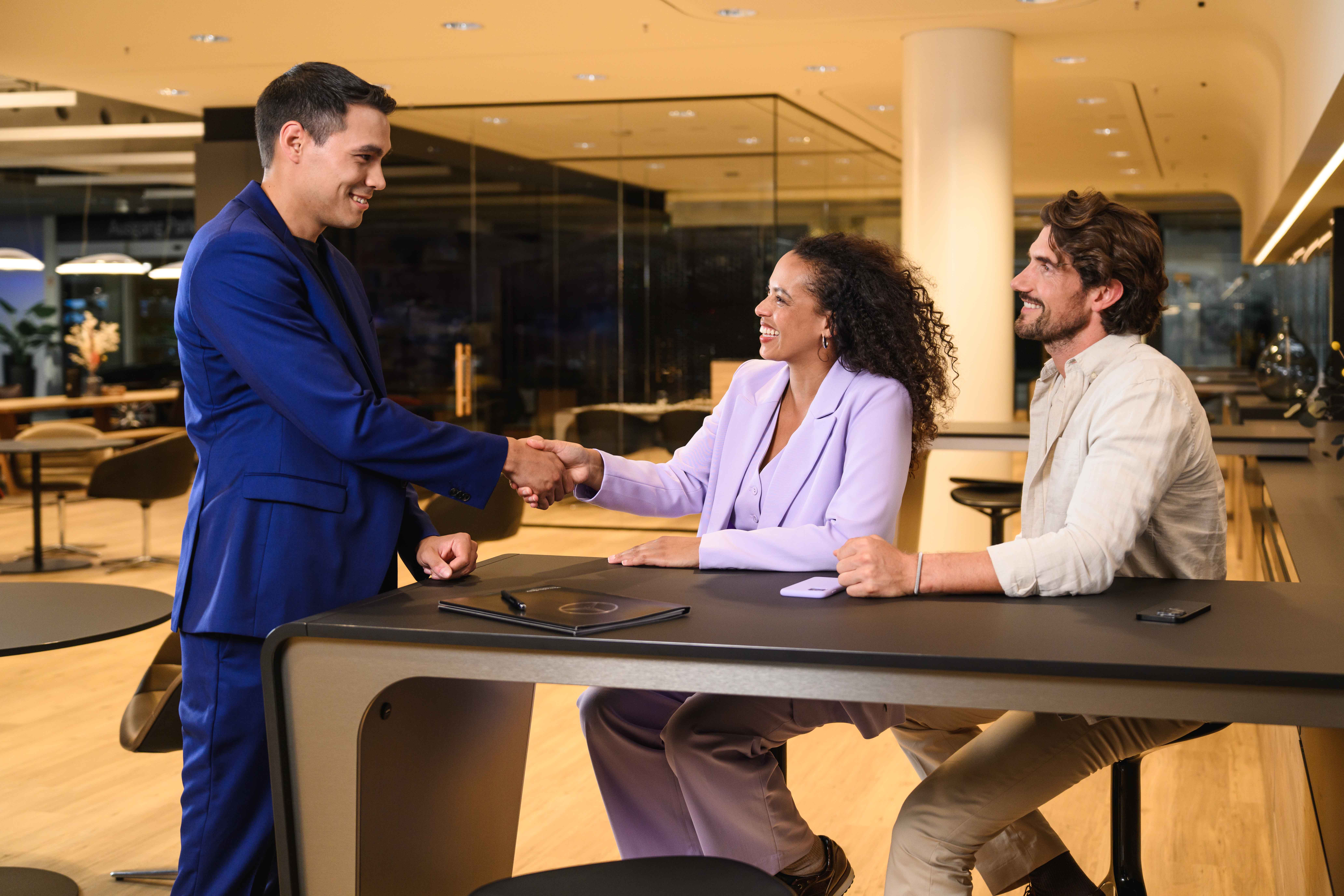 Three colleagues shaking hands across a showroom desk Three colleagues shaking hands across a showroom desk.