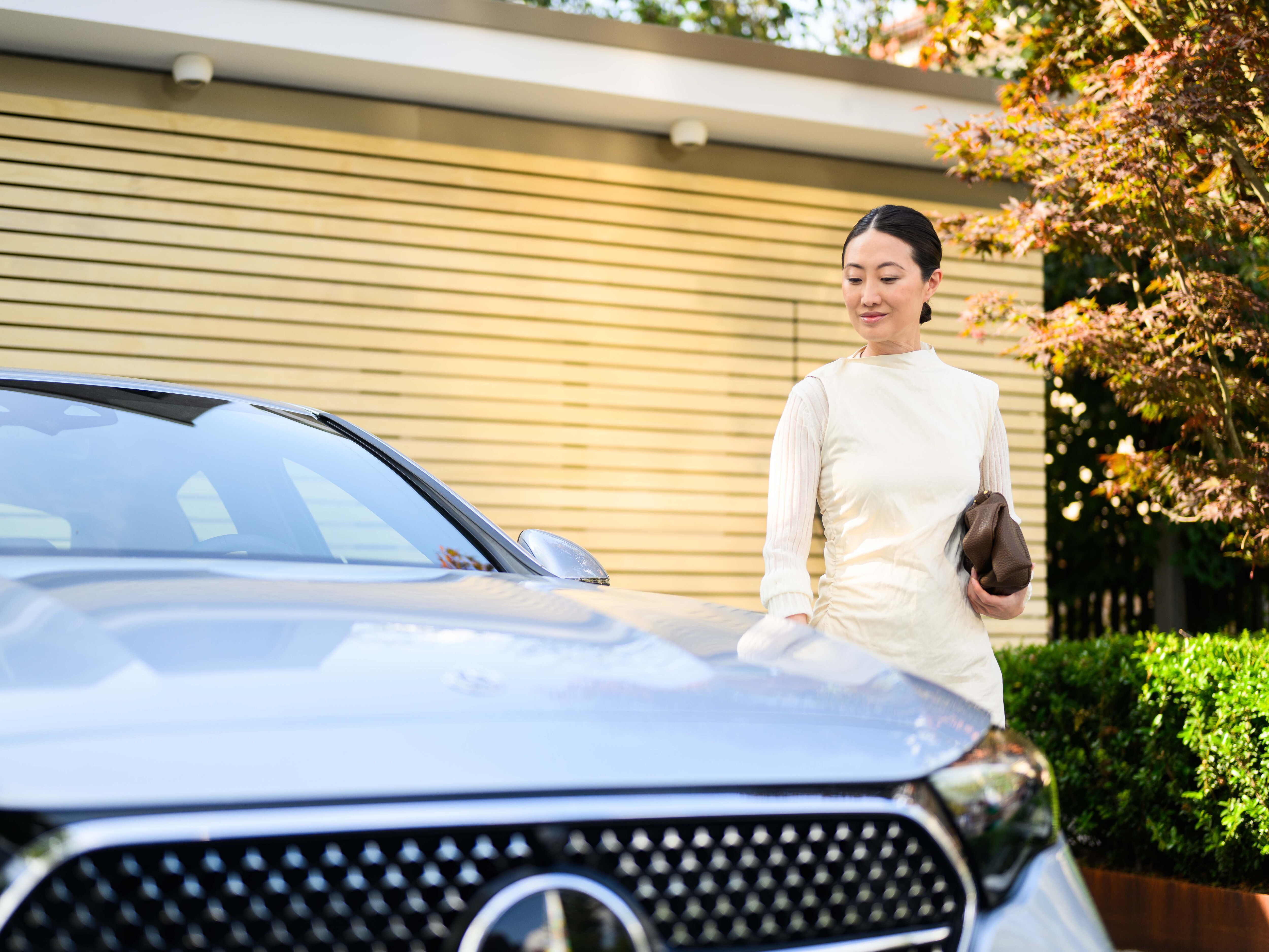 Woman beside a blue Mercedes-Benz outside a home.
