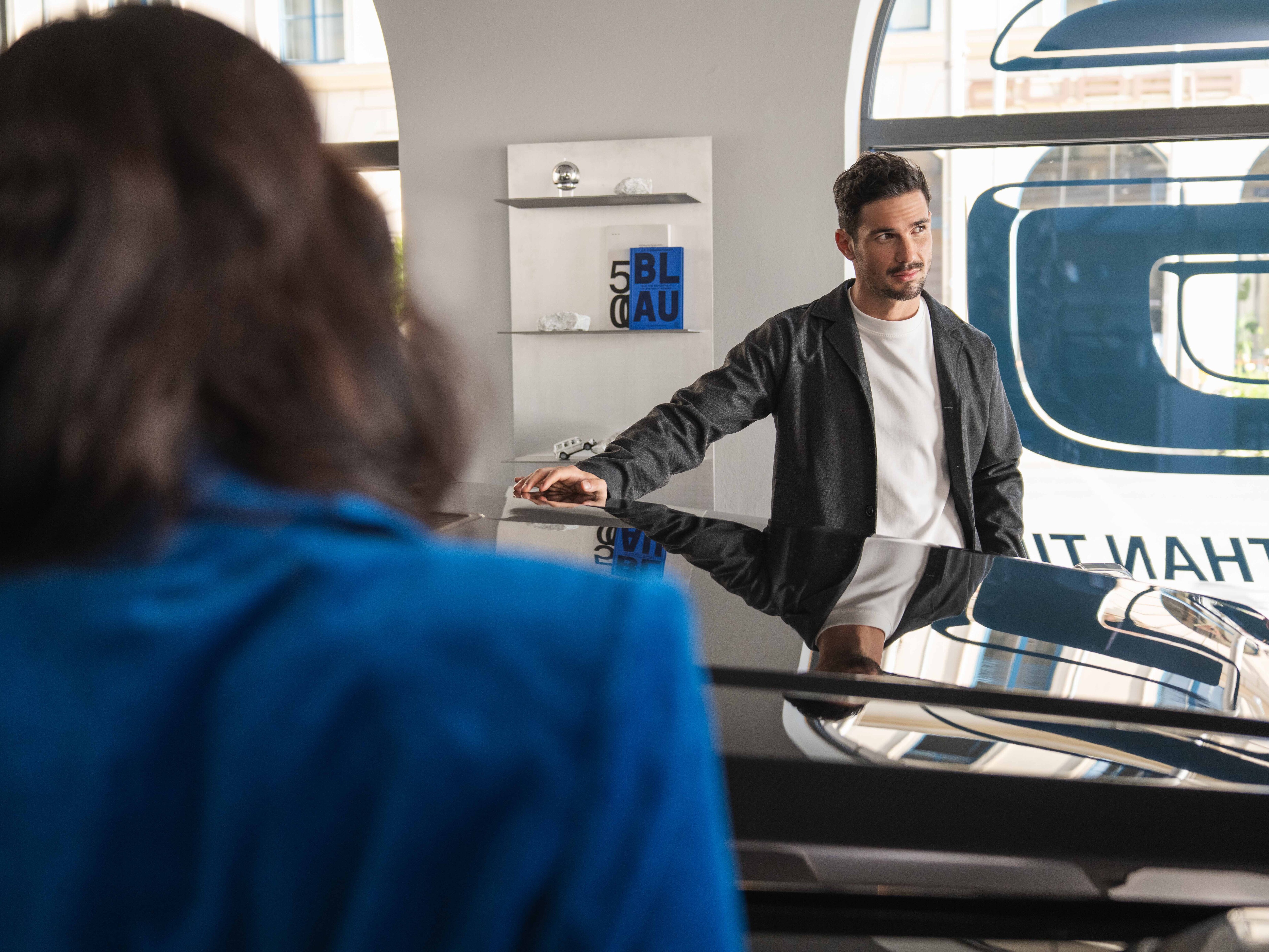 Two people smiling and talking in front of a Mercedes-Benz vehicle.