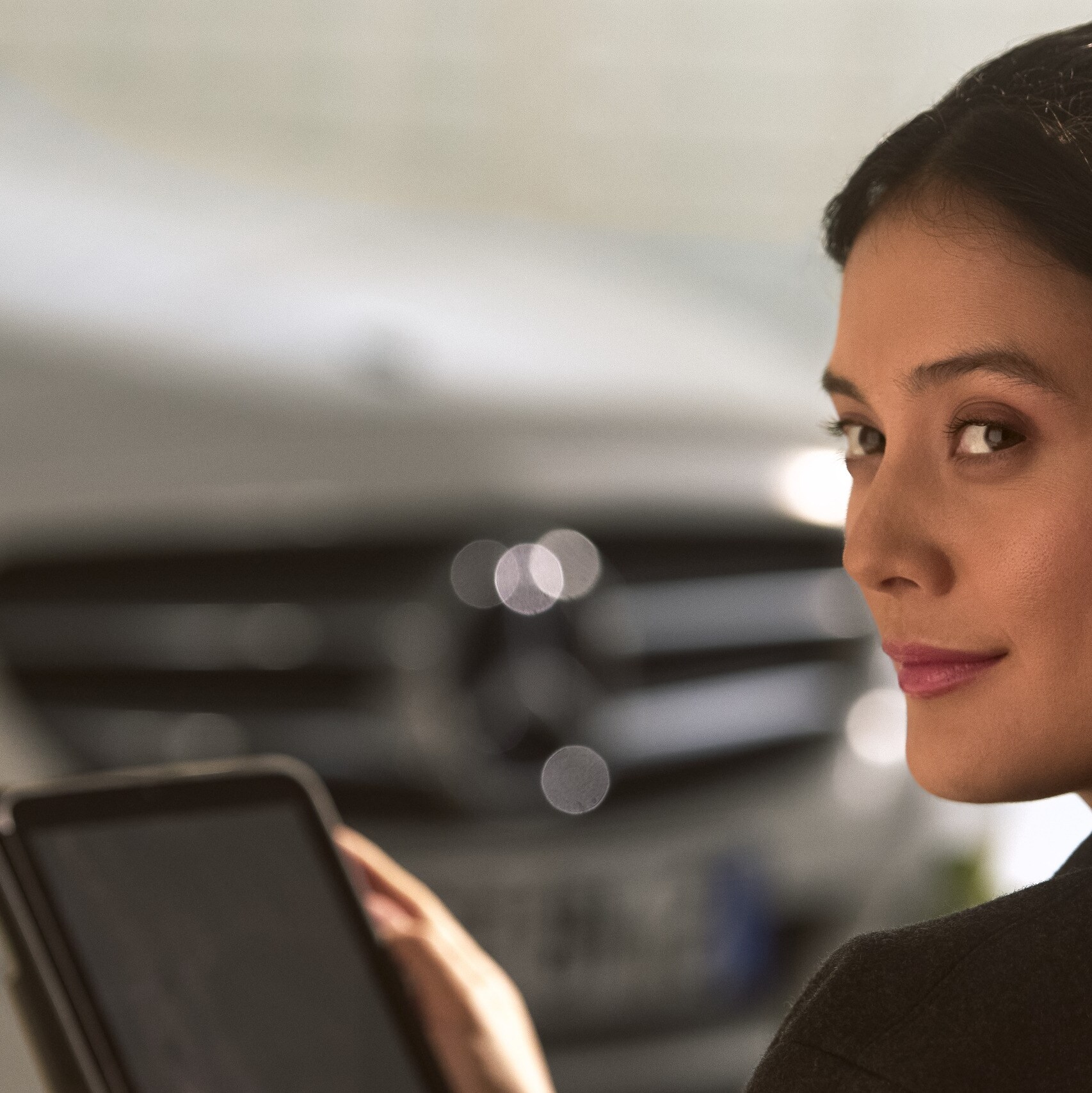 A person holding a tablet in front of a Mercedes-Benz vehicle.
