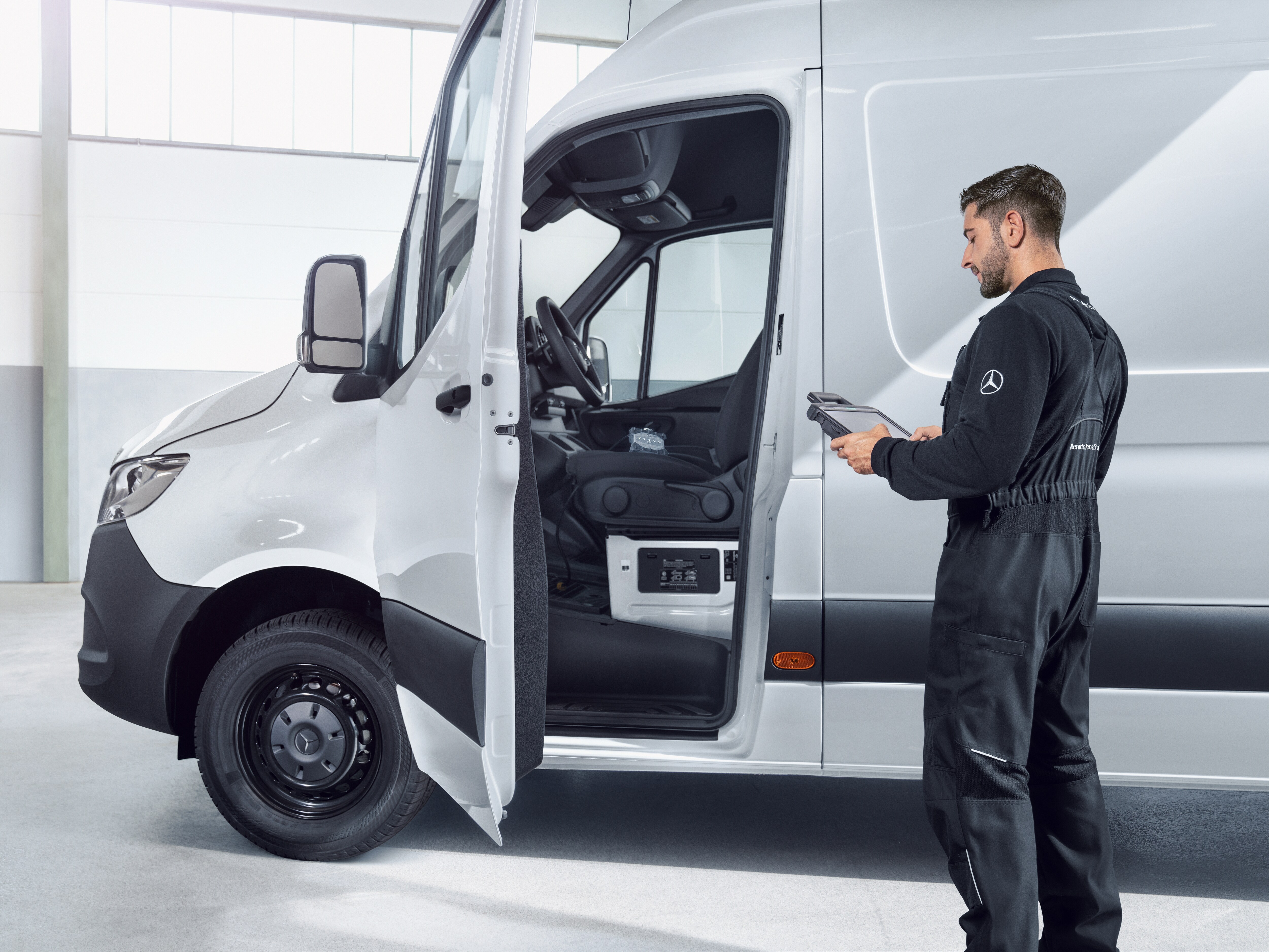 Person standing beside an open Mercedes-Benz van while using a handheld device