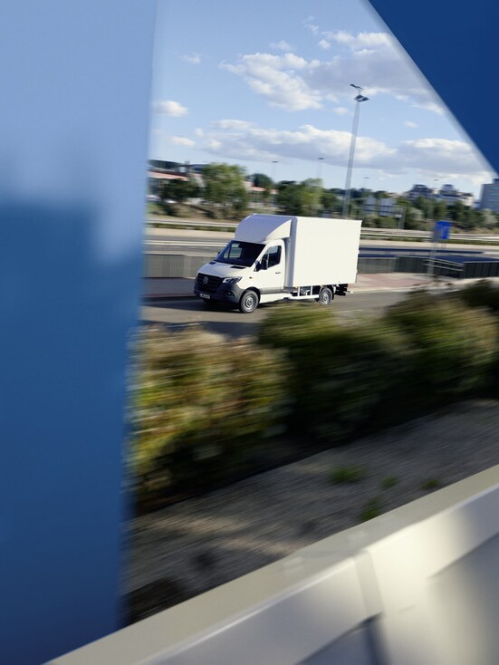 A white Mercedes-Benz eSprinter Luton Box van driving on the road.