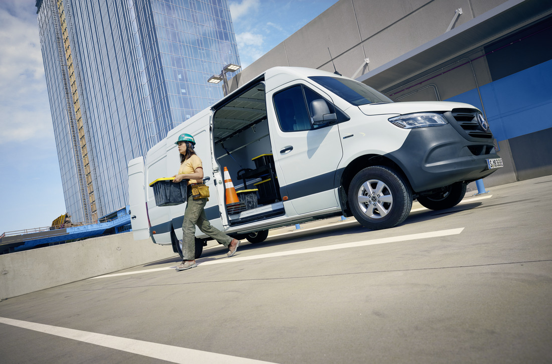 Person Carrying a Box Next to eSprinter Panel Van | Mercedes-Benz Vans A person carrying a box next to a white Mercedes-Benz eSprinter Panel van.