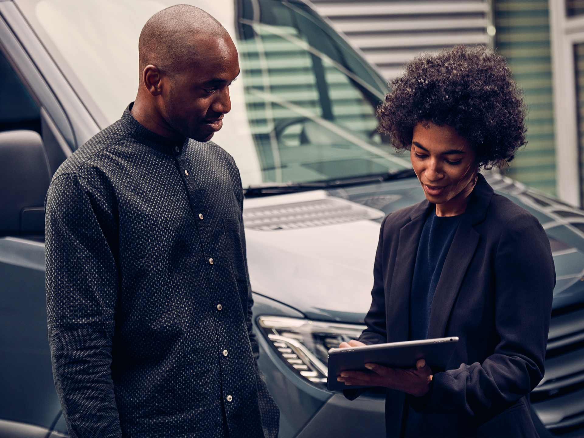 Two people by a Mercedes-Benz van | Mercedes-Benz Vans A man and a woman looking at a tablet together in front of a grey Sprinter van.