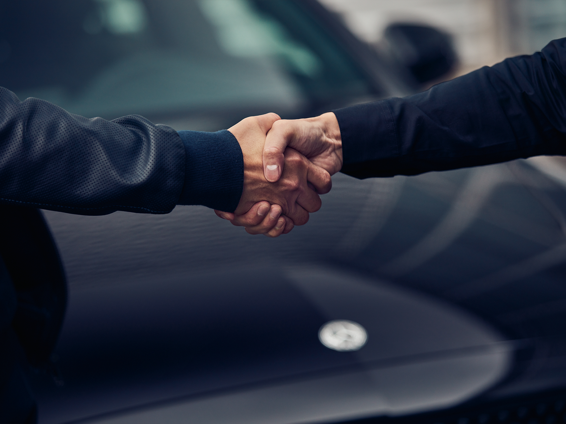 Handshake in front of a Mercedes-Benz van | Mercedes-Benz Vans A close up of two people shaking hands over the bonnet of a dark Mercedes-Benz van.