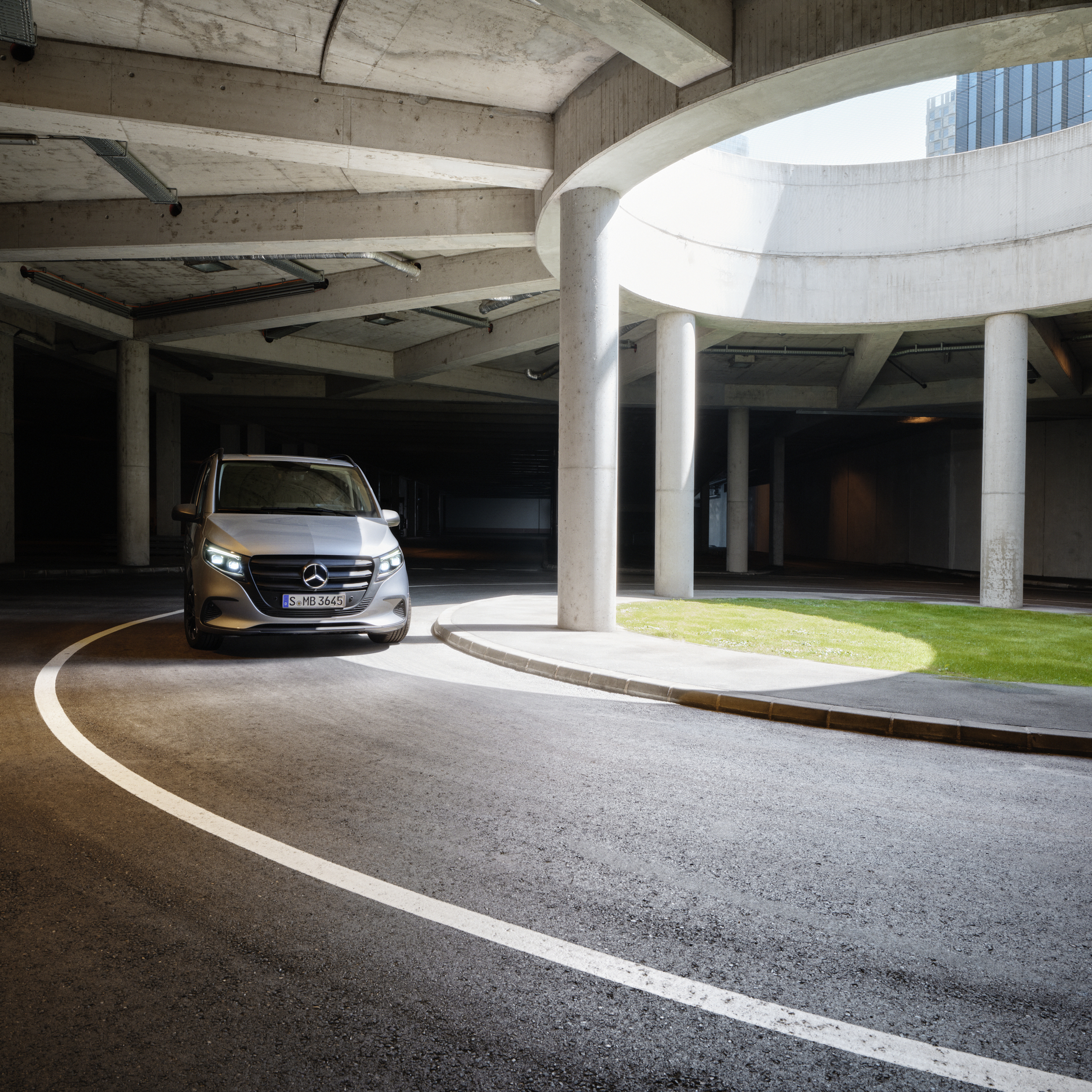 A Silver Mercedes-Benz Van in a Car Park | Mercedes-Benz Vans A silver Mercedes-Benz van driving through a semi-covered car park with concrete pillars and a grass verge.