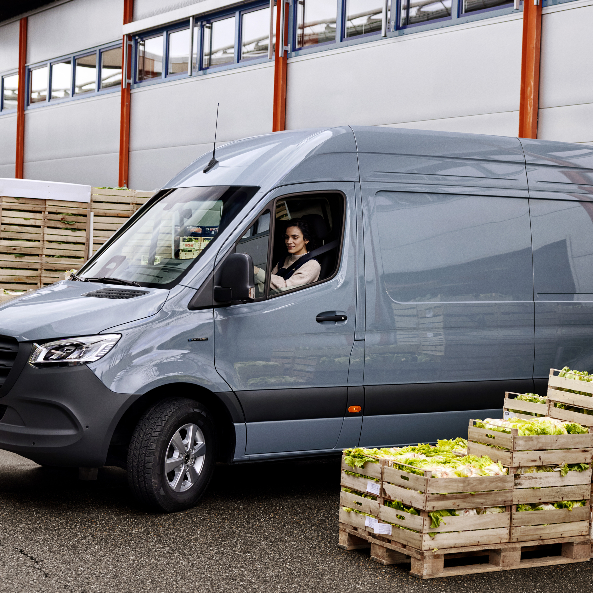 A Woman in a Mercedes-Benz eSprinter Van | Mercedes-Benz Vans A woman sitting in the driver's seat of a grey Mercedes-Benz eSprinter van next to crates of lettuce.