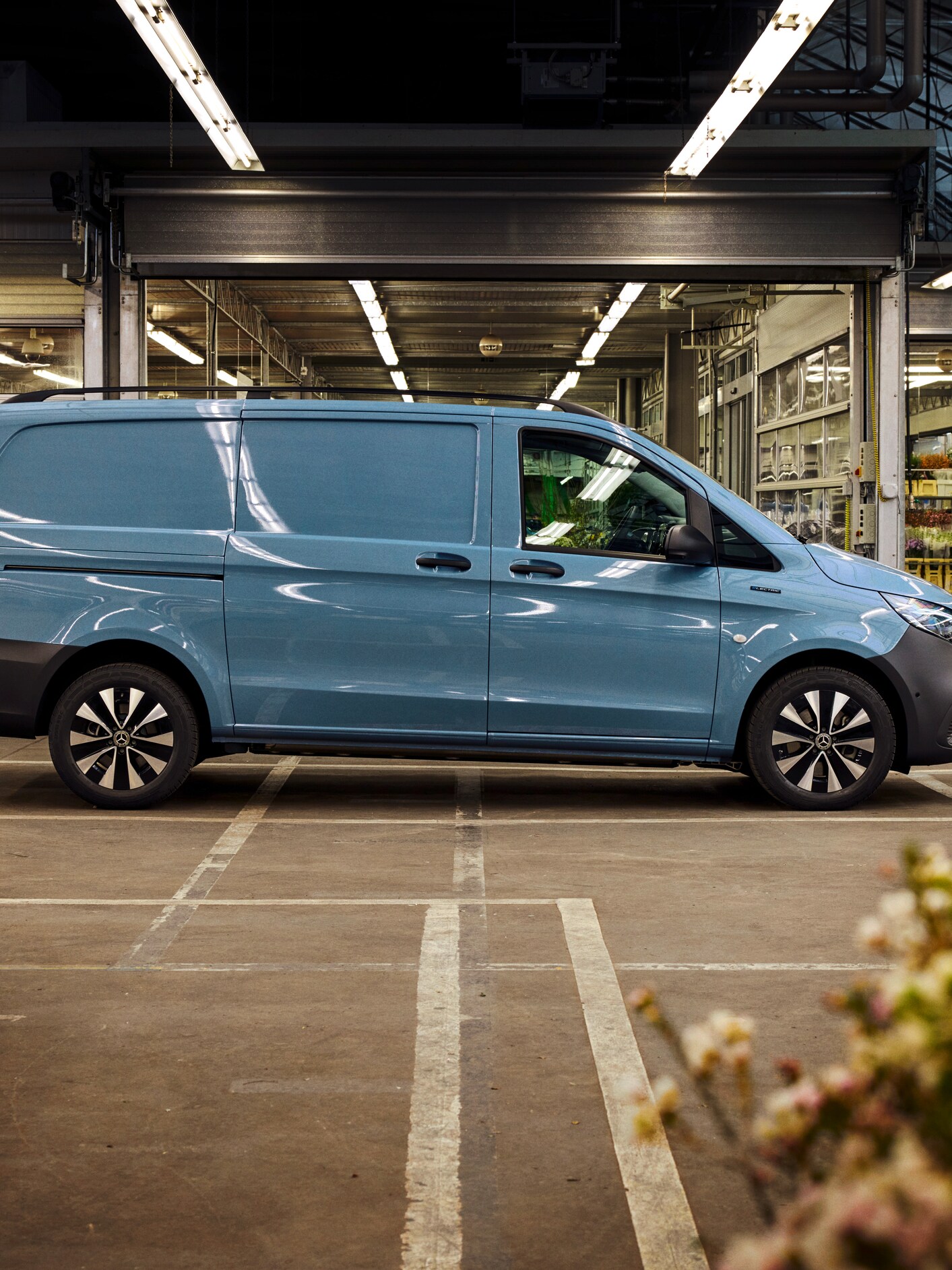 A side view of a blue Mercedes-Benz eVito van in a car park with an open building in the background.