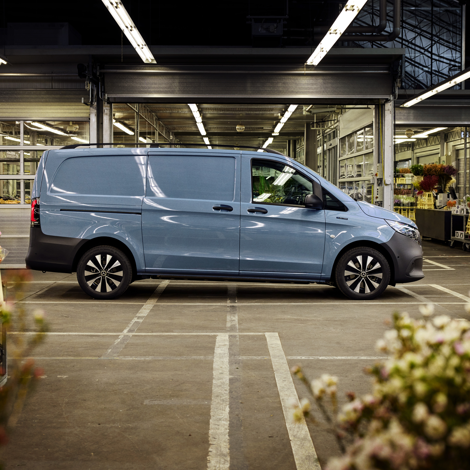 A Blue Mercedes-Benz eVito Van | Mercedes-Benz Vans A side view of a blue Mercedes-Benz eVito van in a car park with an open building in the background.