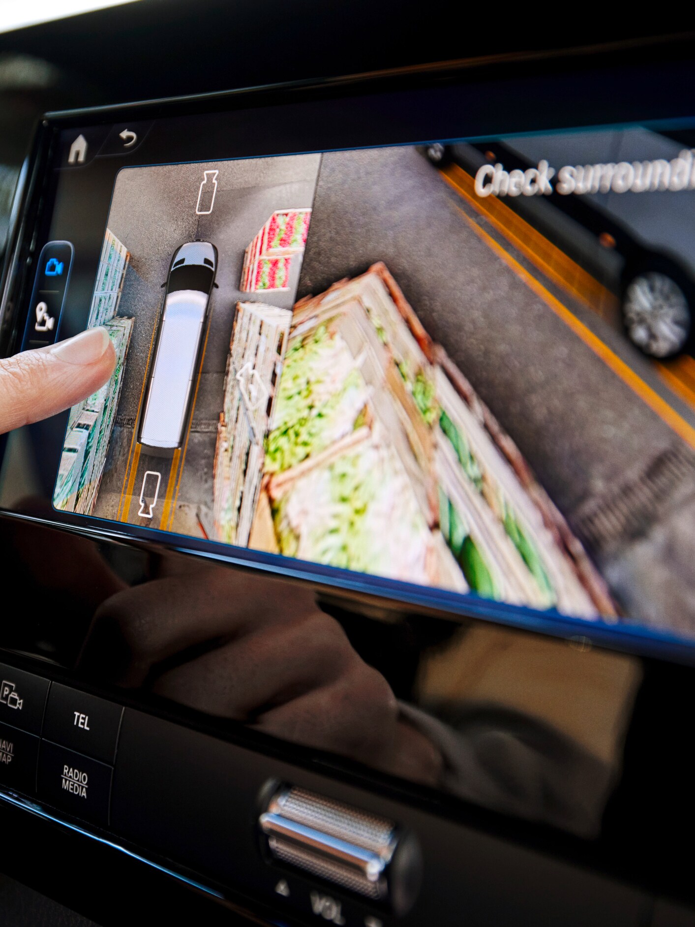 A finger on a vehicle infotainment screen showing a 360-degree top-down camera view.