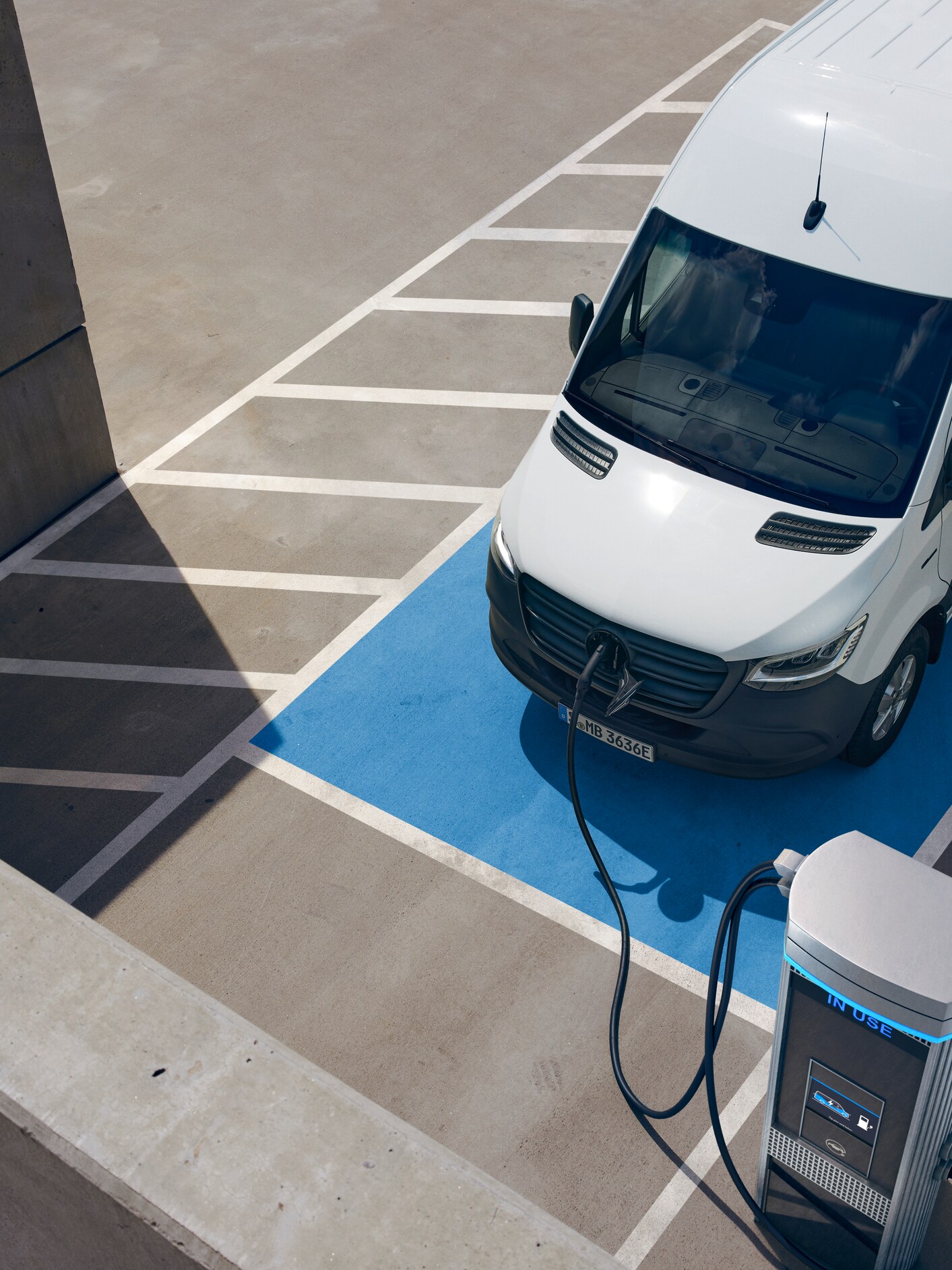 An elevated view of a white Mercedes-Benz van parked and charging at an electric vehicle charging station.