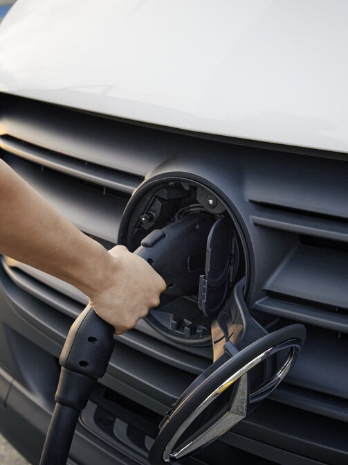 A person plugging a charging cable into the front of a Mercedes-Benz eSprinter electric van.