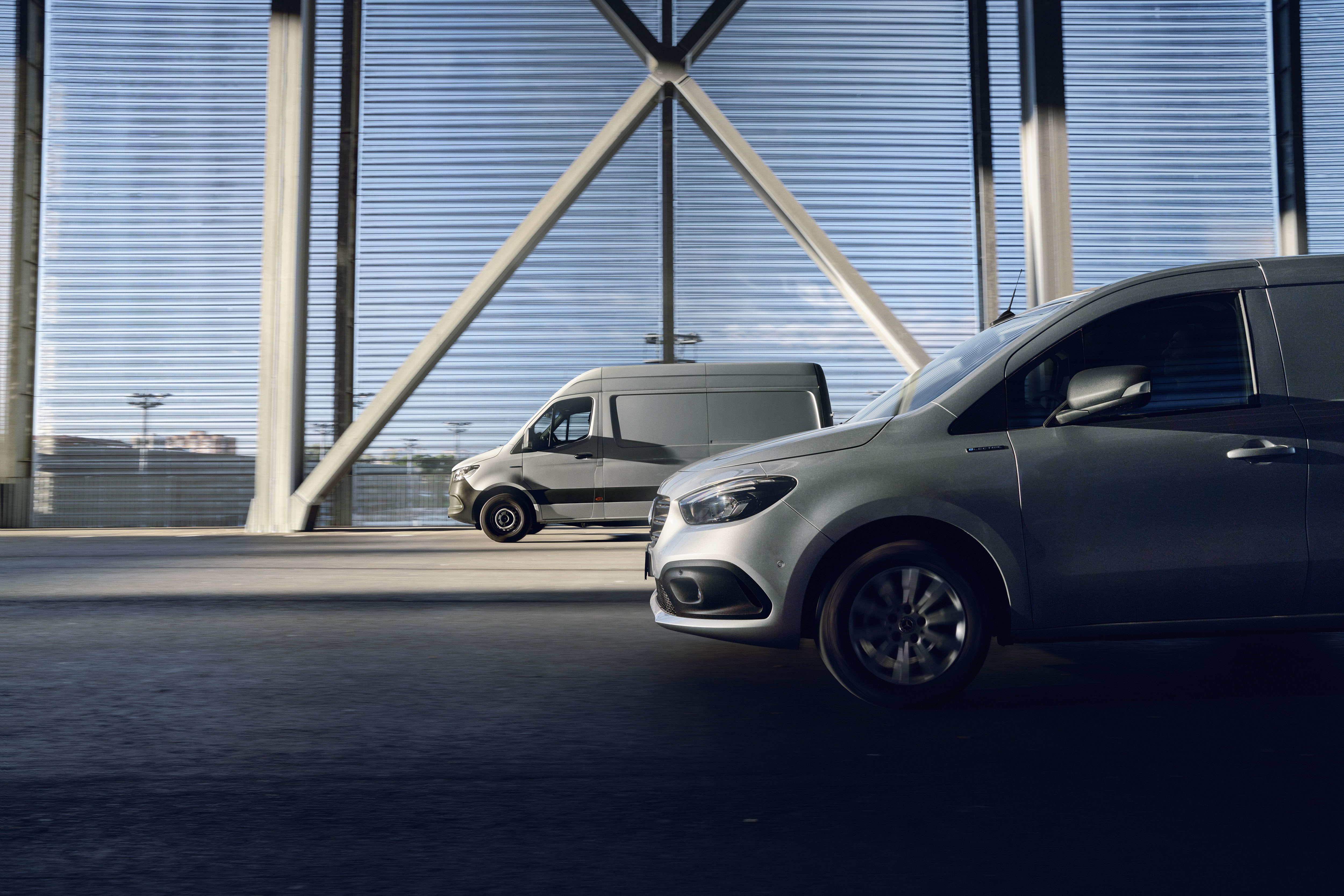 Citan & Sprinter Vans on the Road | Mercedes-Benz Vans Two Mercedes-Benz commercial vehicles: a silver Citan van in the foreground and a grey Sprinter in the background.