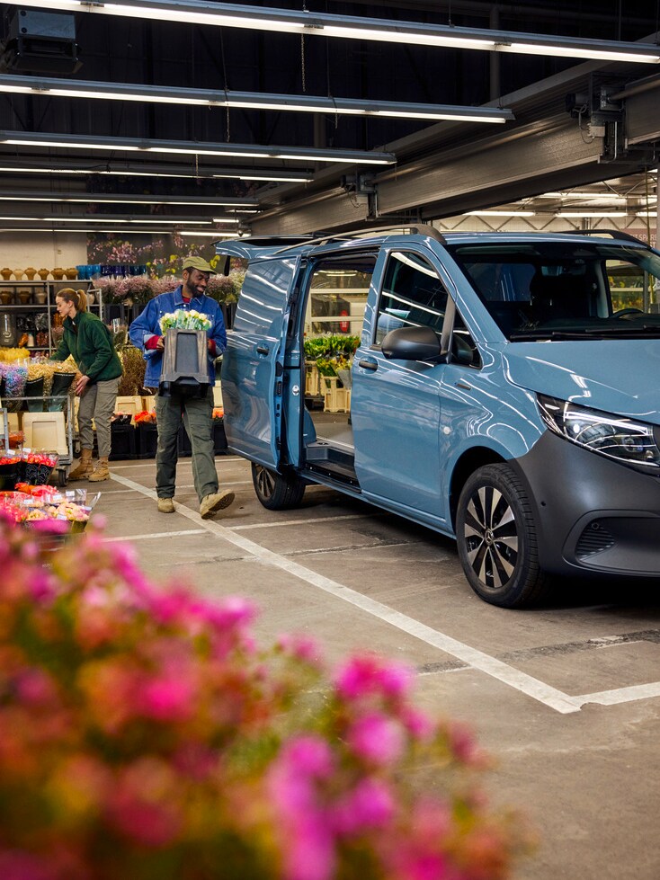 Two people loading flowers into a blue Mercedes-Benz eVito van.
