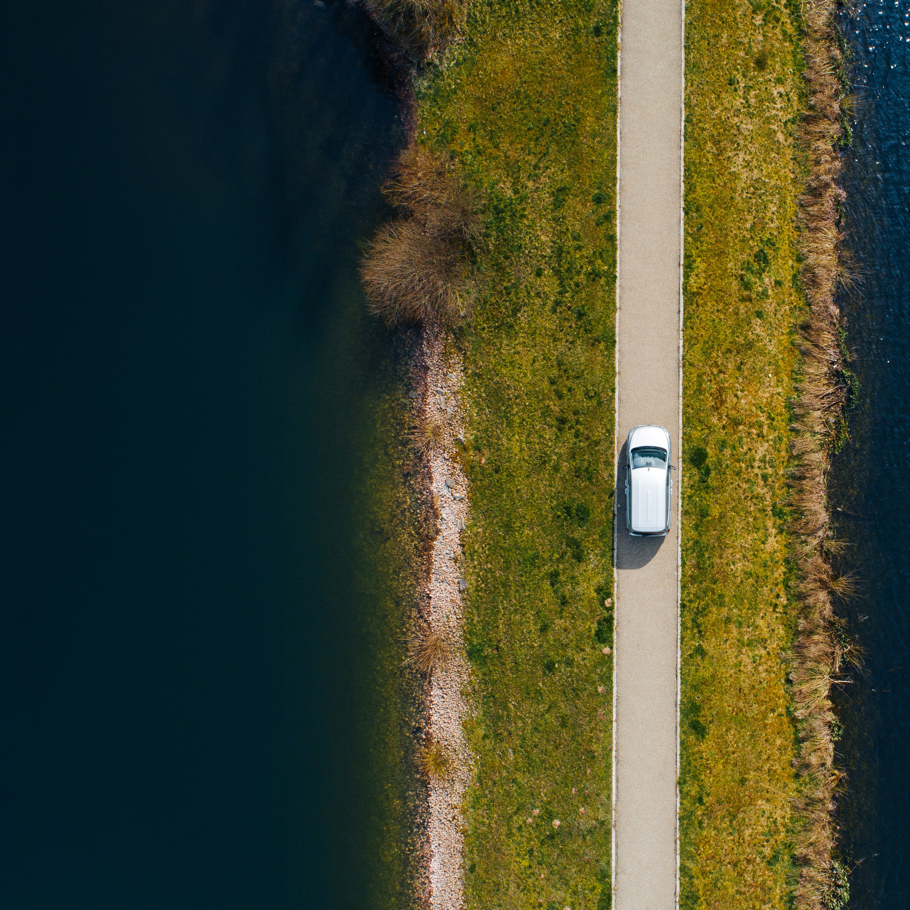 Aerial view of a white Mercedes-Benz van on a narrow road between two bodies of water.