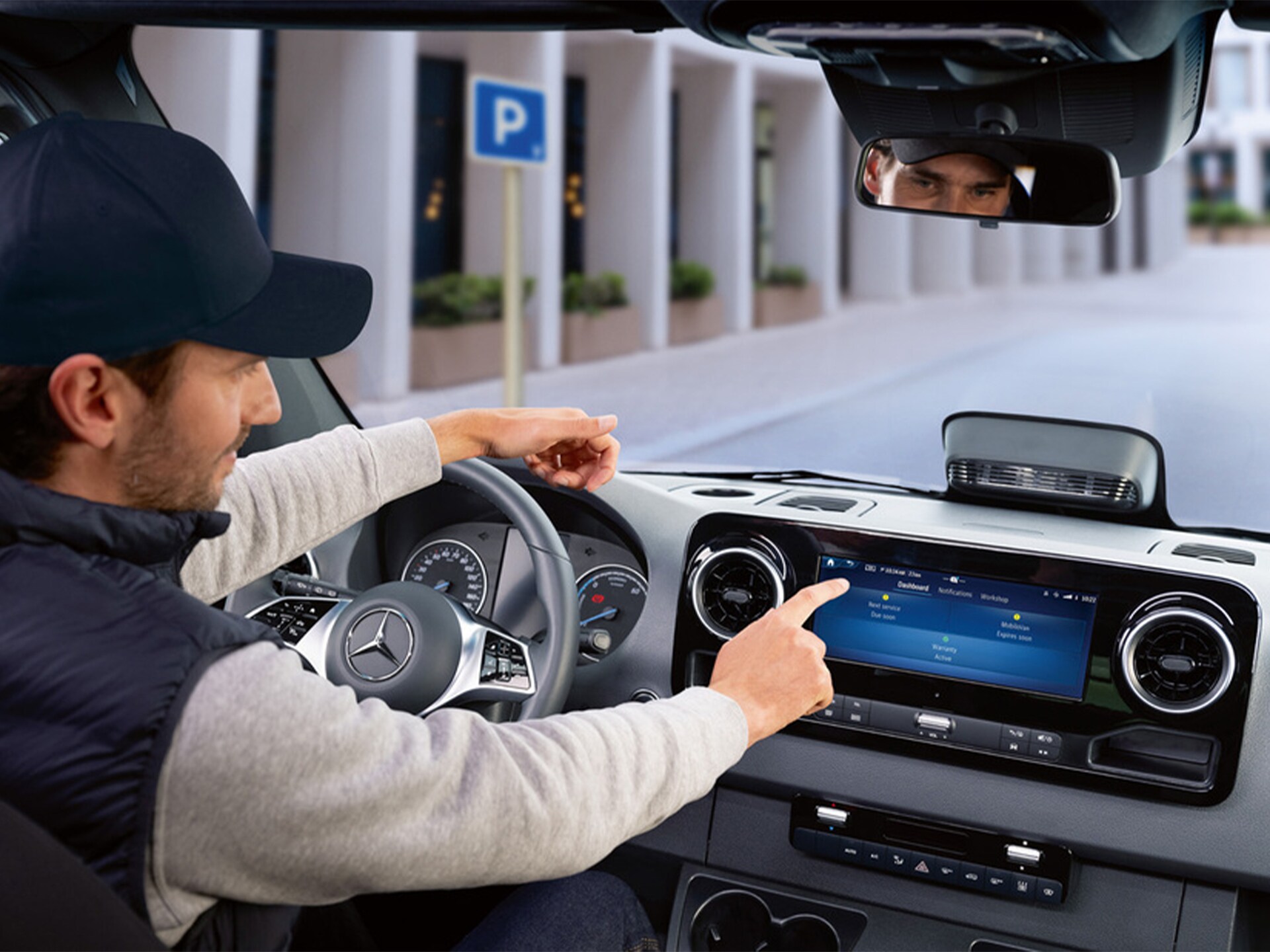 A person operating a Mercedes-Benz vehicle's infotainment system while parked near a designated parking area. 