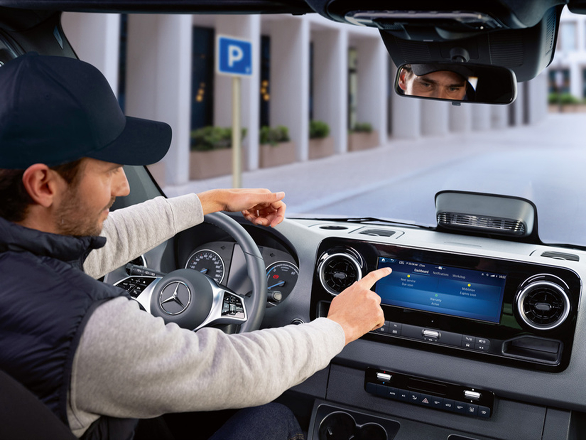 Driver using vehicle infotainment system | Mercedes-Benz Vans A person operating a Mercedes-Benz vehicle's infotainment system while parked near a designated parking area.