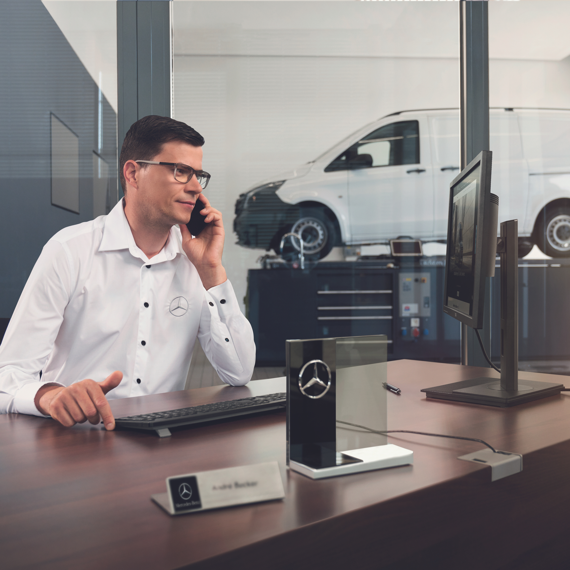 Service Advisor | Mercedes-Benz Vans A Mercedes-Benz service advisor in glasses talking on the phone at his desk with a white van in the background.
