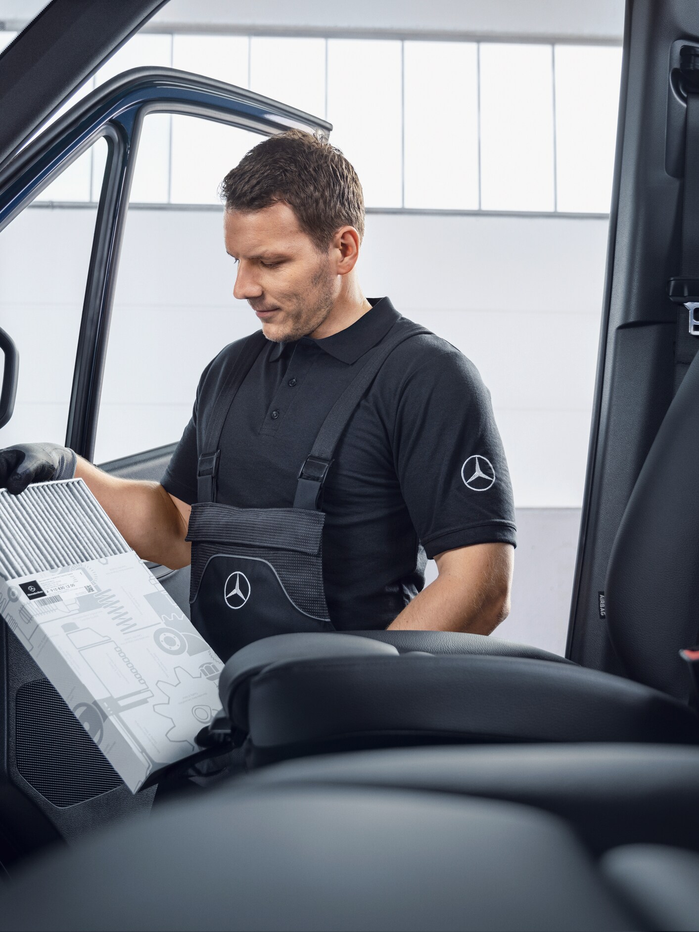 A technician in black uniform examining an air filter in the cabin of a blue Mercedes-Benz van.