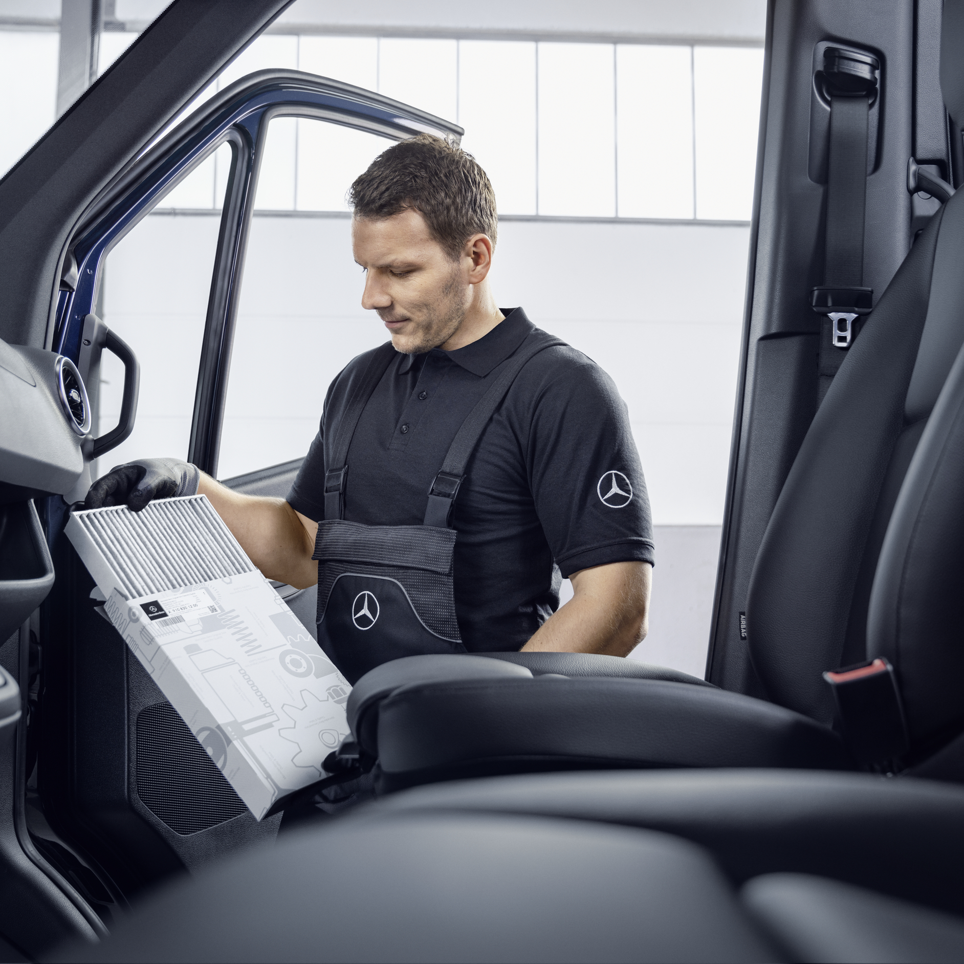 Service Technician | Mercedes-Benz Vans A technician in black uniform examining an air filter in the cabin of a blue Mercedes-Benz van.