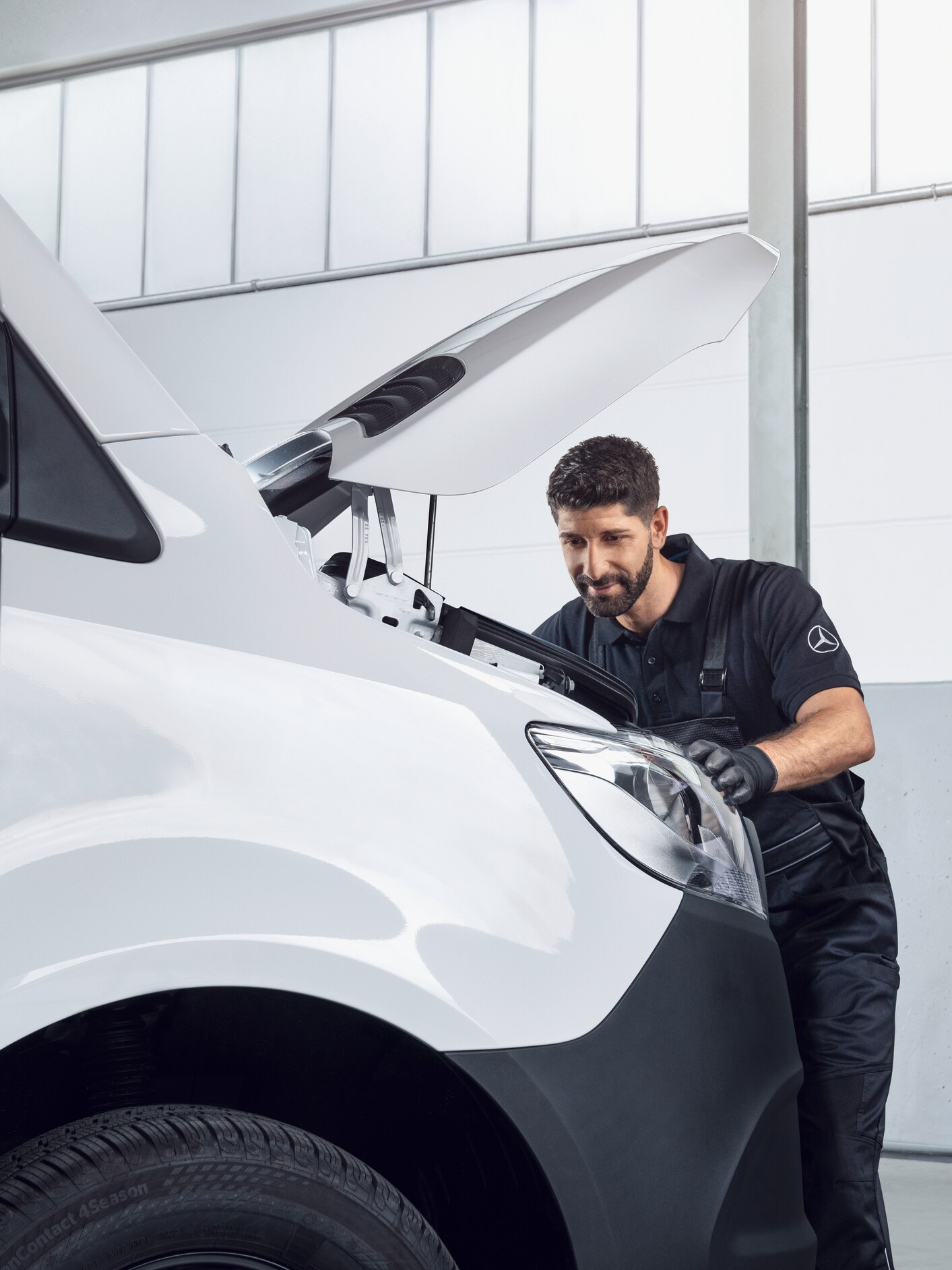 A technician inspecting the engine bay of a white Mercedes-Benz van with the bonnet open.