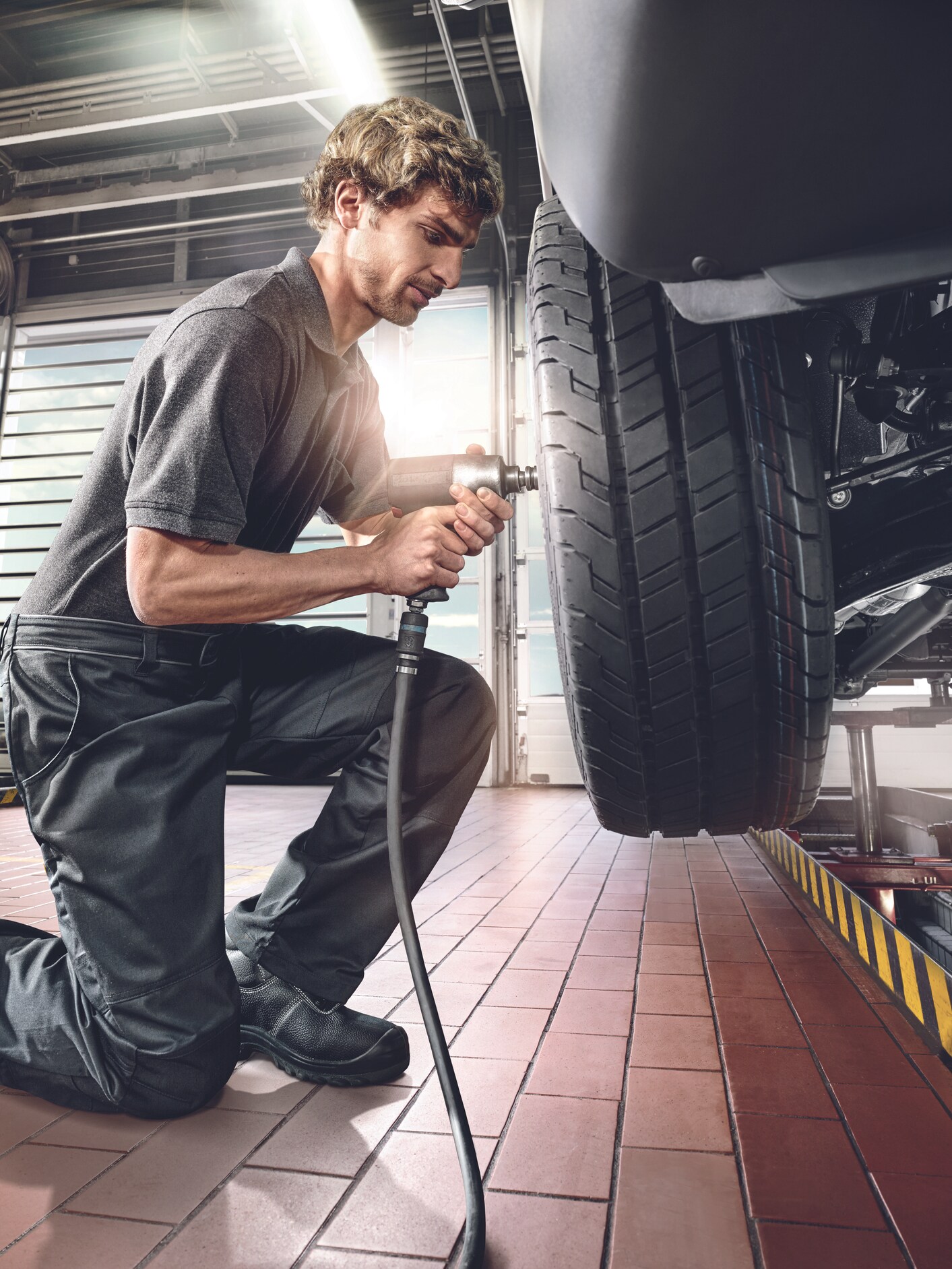 A technician using an impact wrench to change a tyre on a vehicle raised on a lift