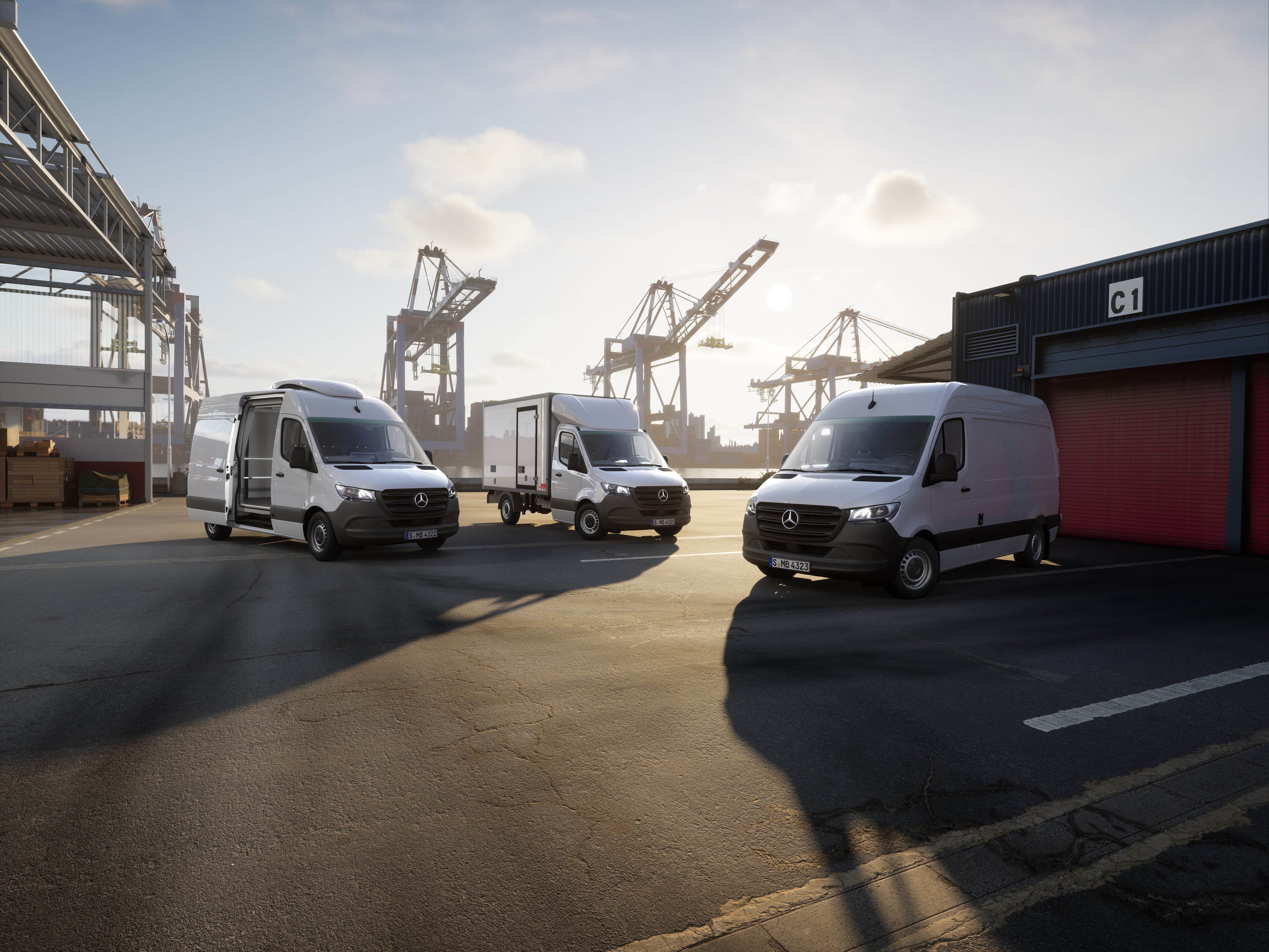 A low-angle shot of three white Mercedes-Benz Sprinter vans parked in a port area.