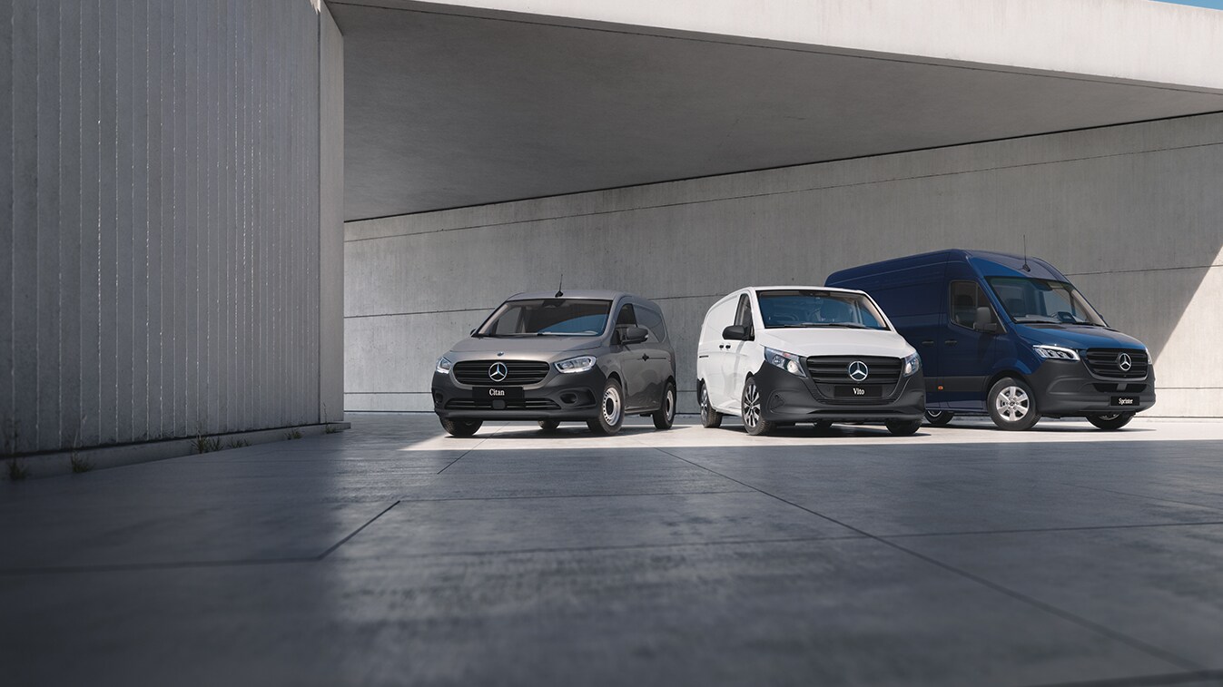 Three Mercedes-Benz panel vans – a grey Sprinter, a blue Vito, and a yellow Citan – positioned on a rooftop with a cityscape backdrop.
