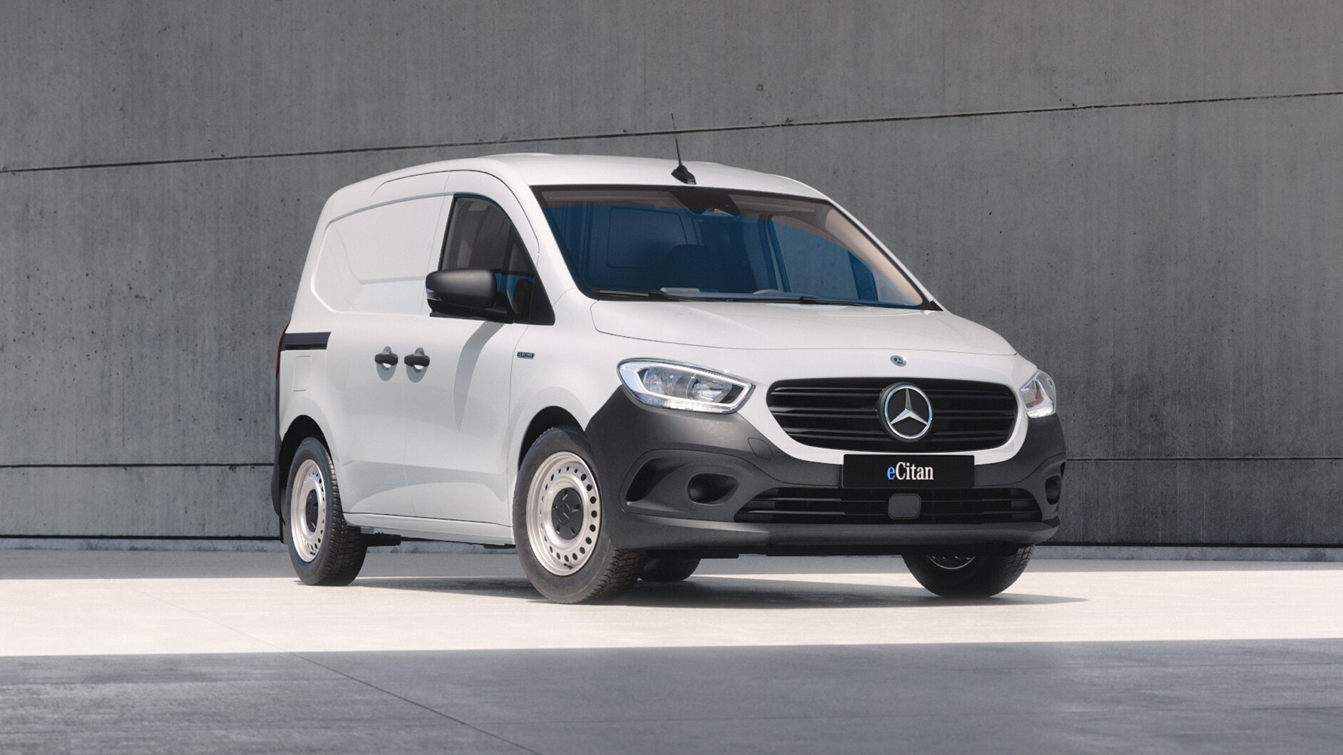 White Mercedes-Benz eCitan Panel Van parked by modern concrete structure.