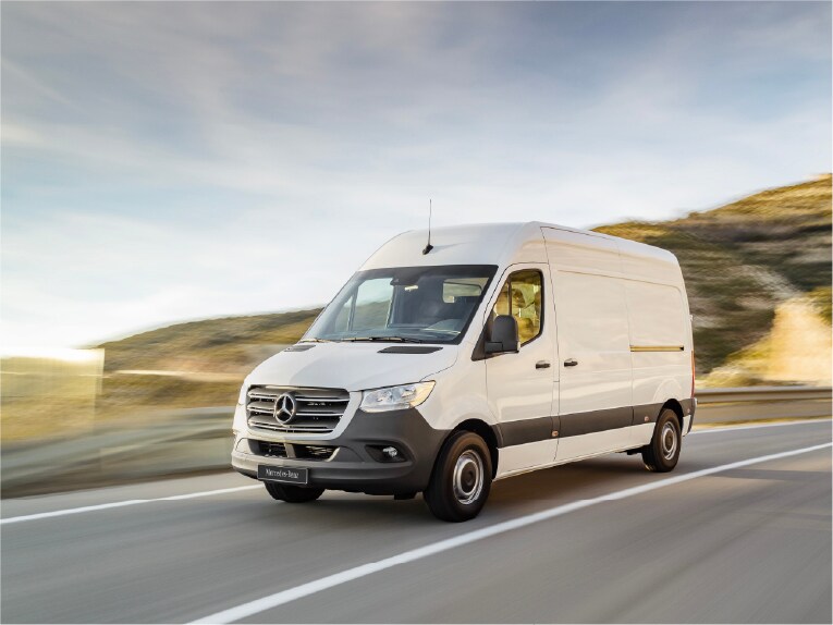 White Mercedes-Benz Sprinter van on a hill road.