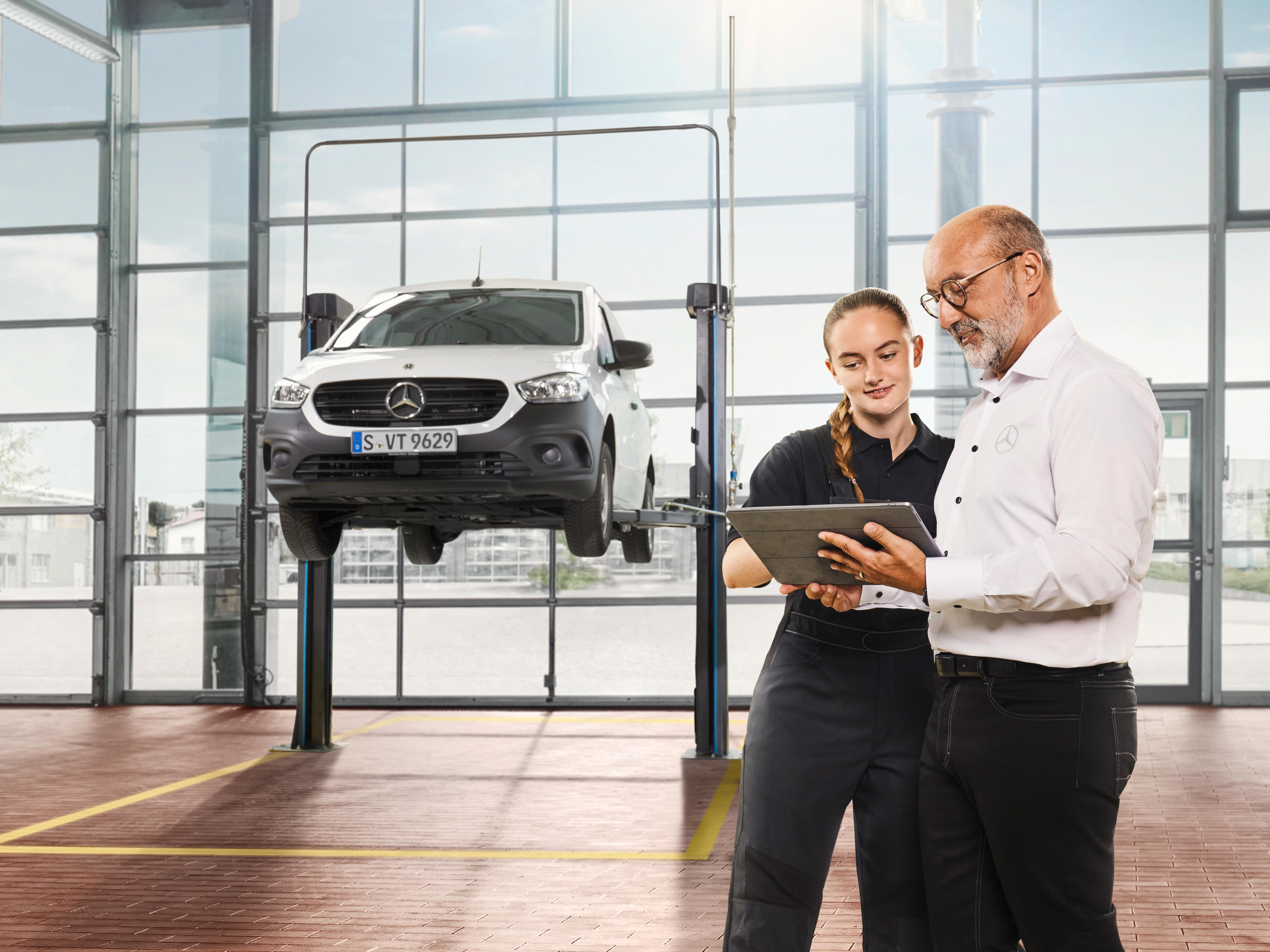 Two people reviewing vehicle servicing information on a tablet in a Mercedes-Benz workshop