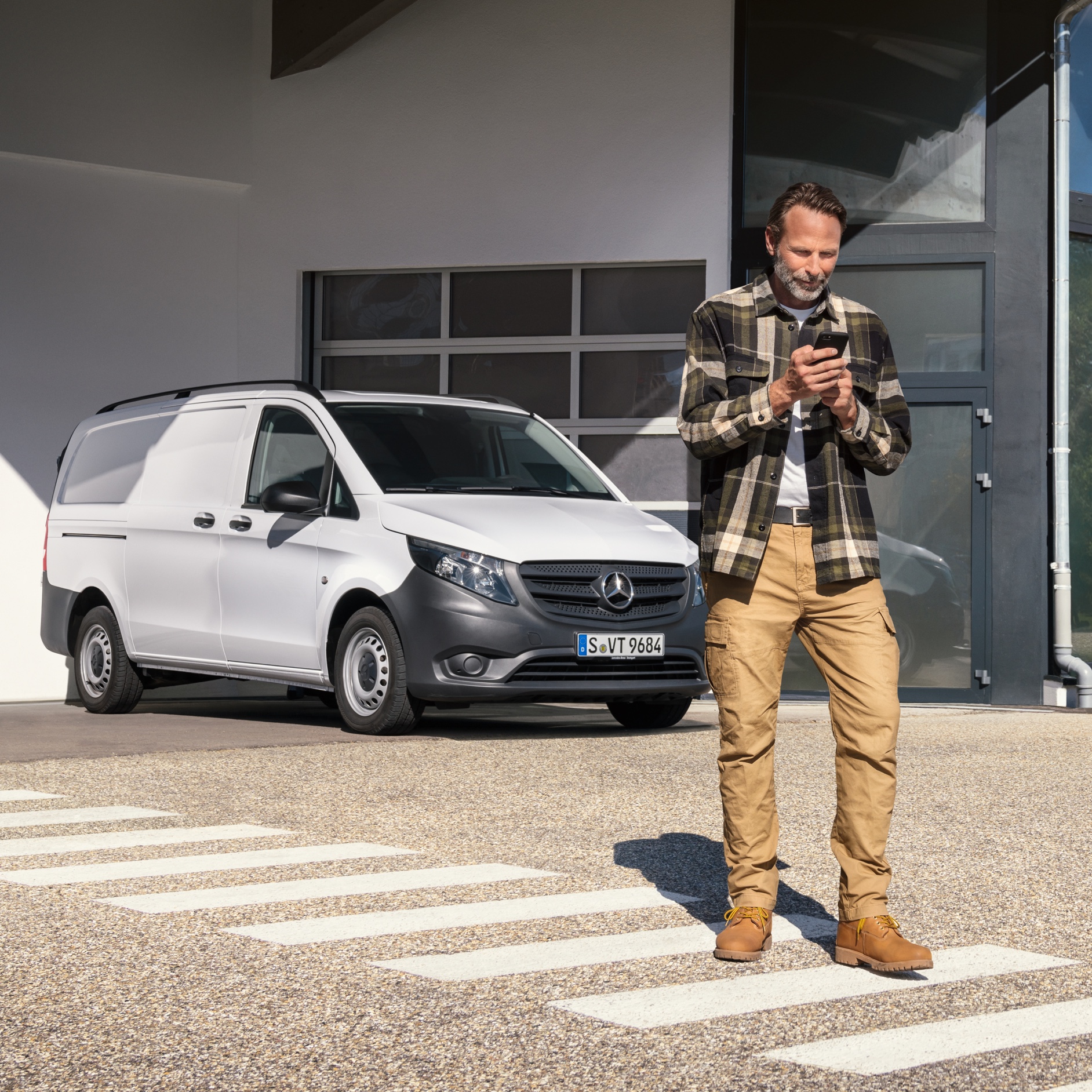 A man standing in front of a white Mercedes-Benz Vito van using his phone. A man standing in front of a white Mercedes-Benz Vito van using his phone.